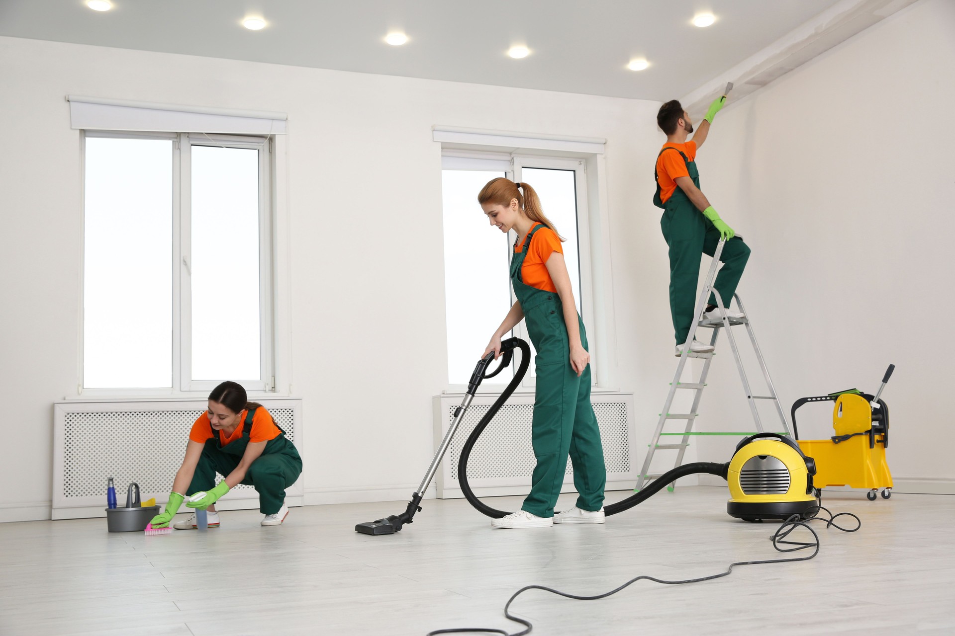 Team of professional janitors in uniforms cleaning room